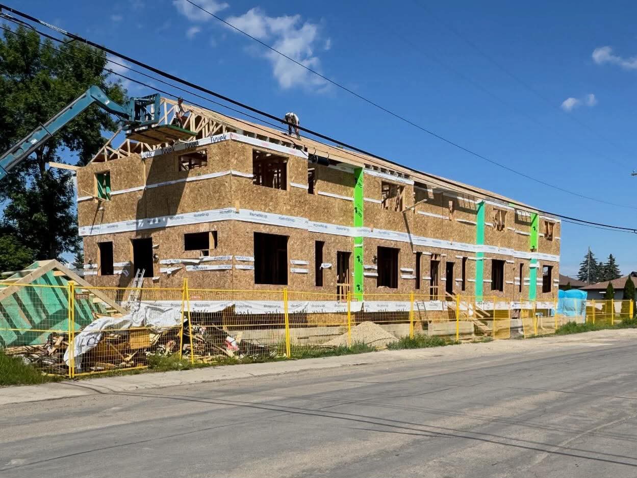 Two-storey wood-framed building under construction with workers on roof trusses